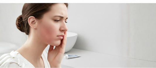 Une femme de profil exprime une vive douleur, la main posée sur sa joue droite qui présente un gonflement rouge (chique dentaire).