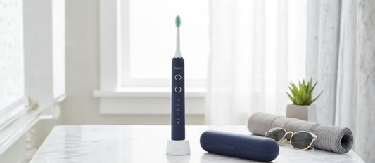 Brosse à dents sonique Nomad bleu marine sur un comptoir en marbre avec son étui de voyage, illustrant l'alliance entre technologie de pointe et mobilité.
