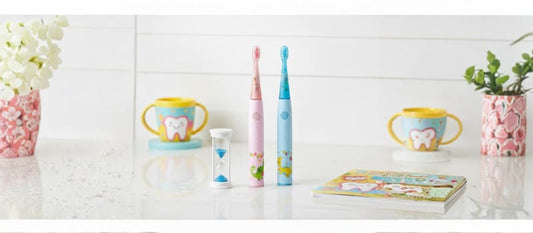 Deux brosses à dents électriques pour enfants, une rose et une bleue avec des motifs de dinosaures, posées sur un plan de travail blanc