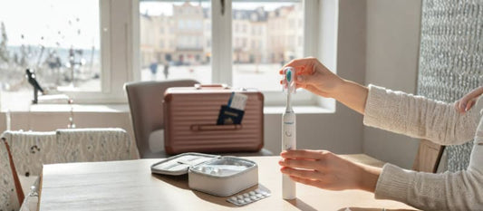 Brosse à dents sonique Nomad sur une table en bois avec une valise, un passeport et un kit de secours dentaire, illustrant la prévention des urgences dentaires en voyage.